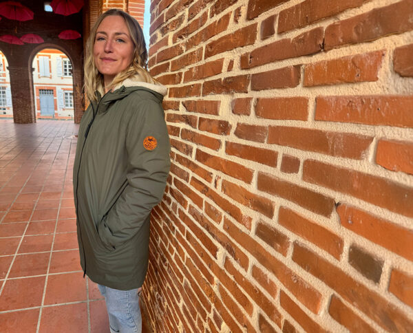 Femme adossée à un mur en briques portant une parka outdoor écoresponsable