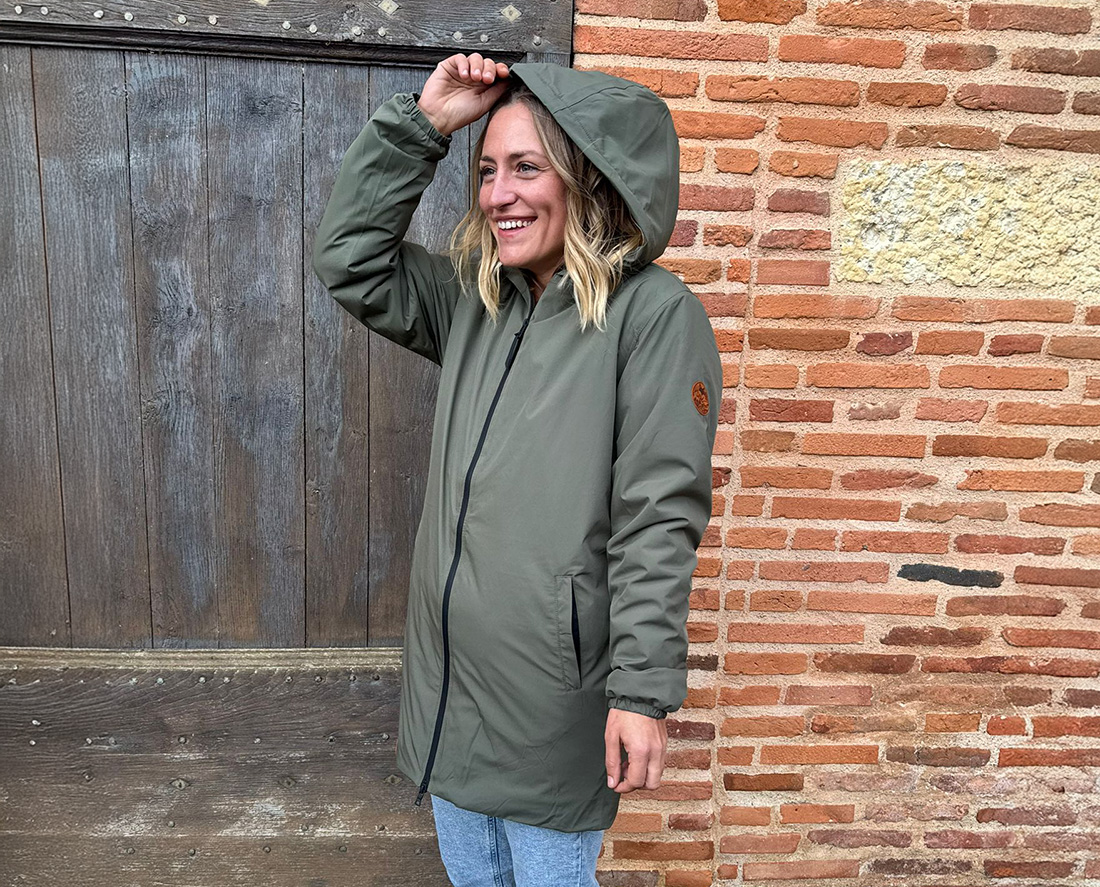 Femme souriante en parka verte à capuche, vêtement outdoor lifestyle durable