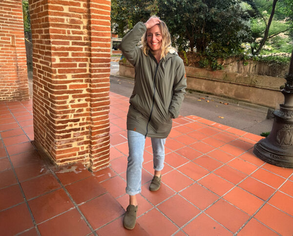 Femme portant une parka verte écoresponsable marchant sur des pavés, style outdoor urbain