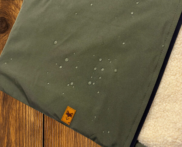 Détail la parka avec zoom sur tissu vert avec patch logo, finition textile responsable doublé sherpa