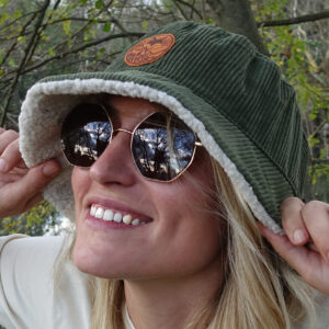 Femme souriante portant un bob en velours cotelé reversible sherpa en forêt.