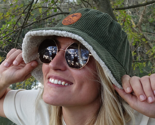 Femme souriante portant un bob en velours cotelé reversible sherpa en forêt.