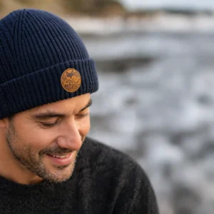 homme portant un bonnet en laine de merinos bleu avec le patch van life en suedine en bord de mer