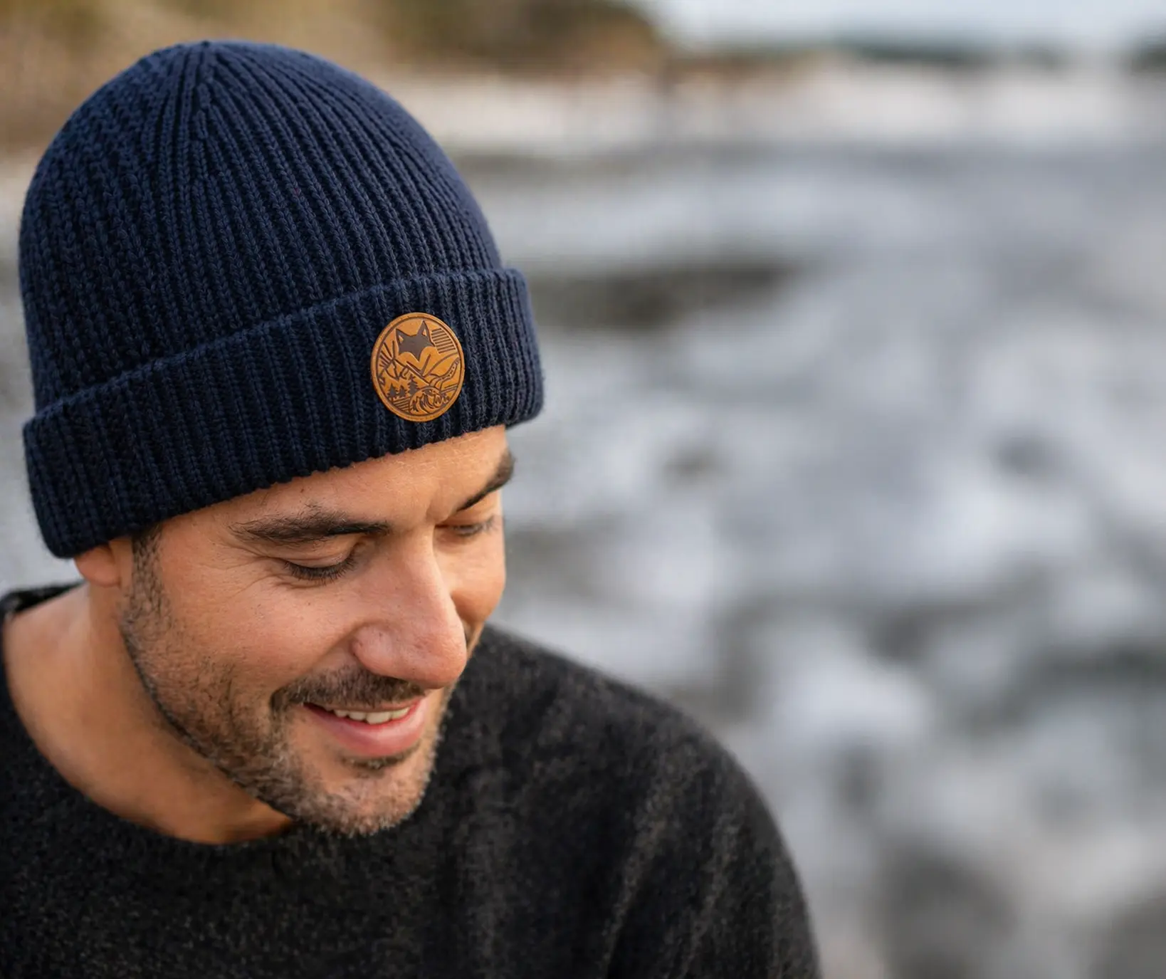 homme portant un bonnet en laine de merinos bleu avec le patch van life en suedine en bord de mer