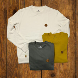 Sweats pliés aux tons naturels présentés sur fond bois, collection outdoor durable