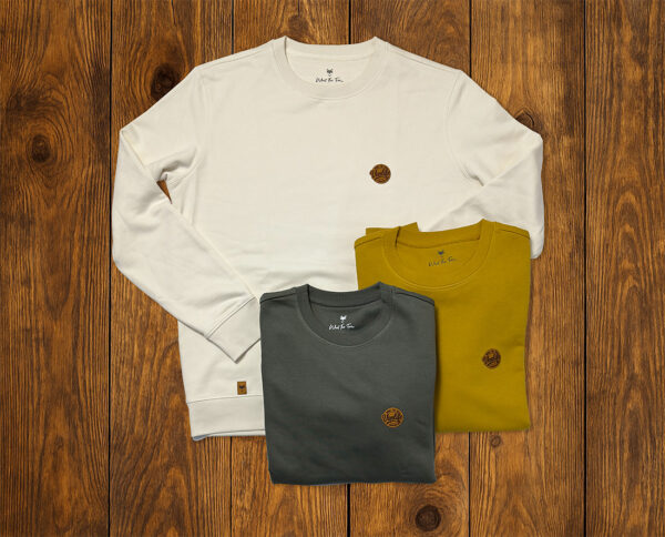 Sweats pliés aux tons naturels présentés sur fond bois, collection outdoor durable