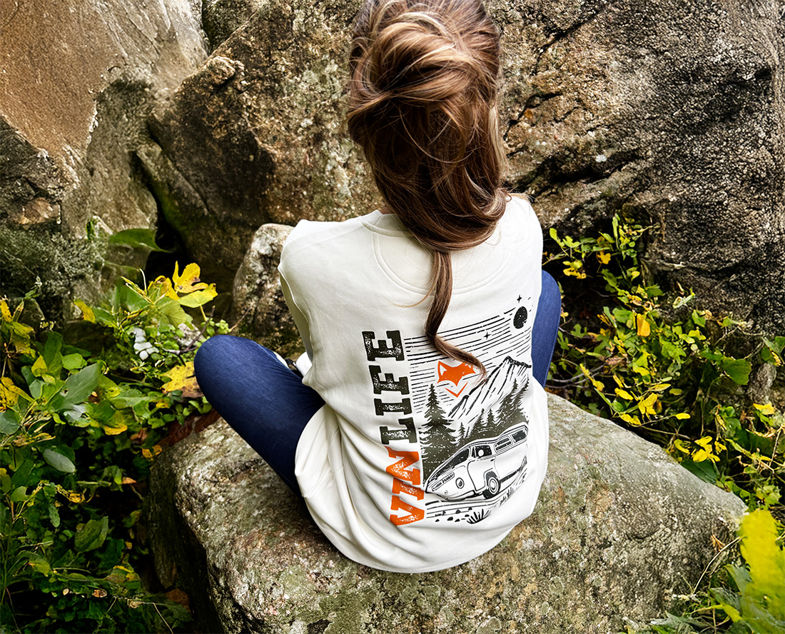 Femme assise sur un rocher portant un sweat vanlife, moment calme en pleine nature