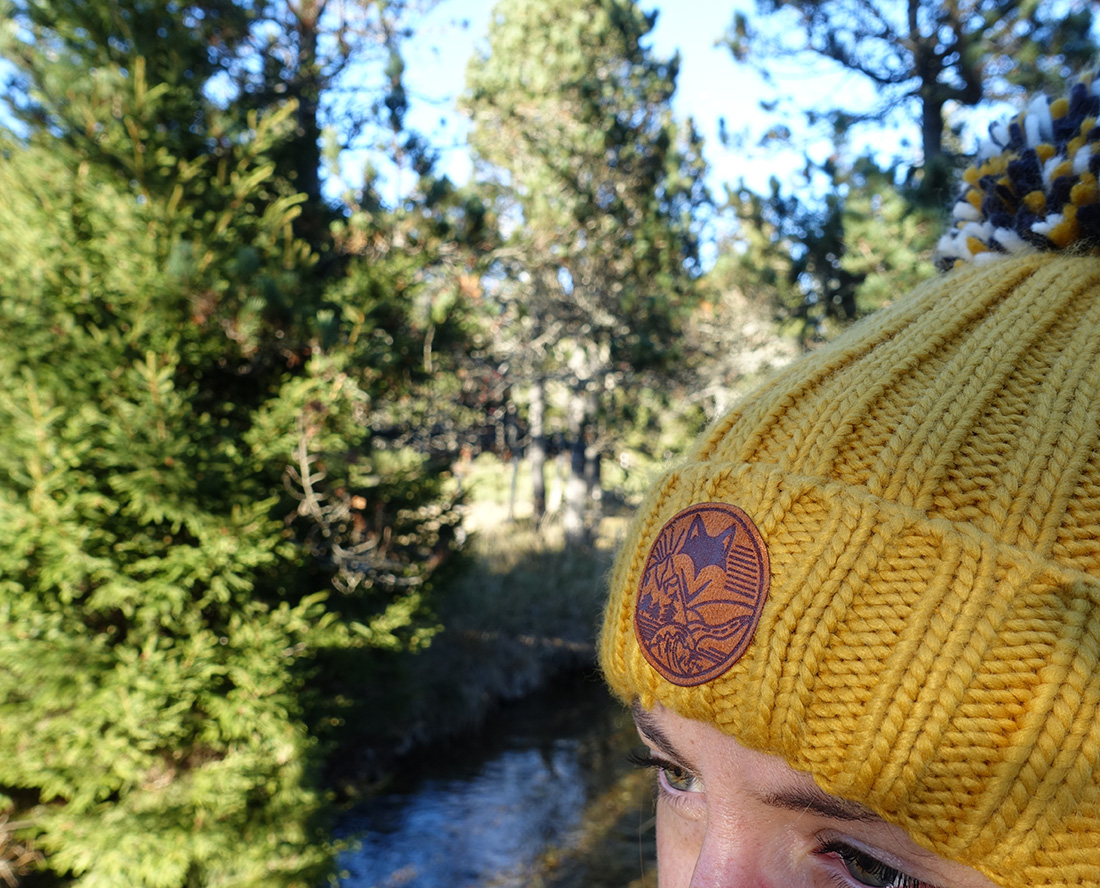 Zoom sur écusson sur bonnet Paysage naturel de rivière en forêt, esprit aventure et vanlife.