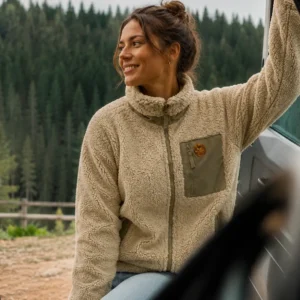 Femme portant une veste sherpa beige devant une forêt, inspiration van life