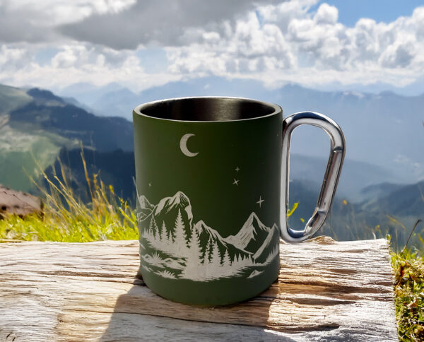 Tasse mousqueton vanlife posée sur un bout de bois devant un paysage naturel