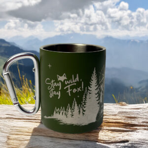 Tasse mousqueton vanlife posée sur un bout de bois devant un paysage naturel