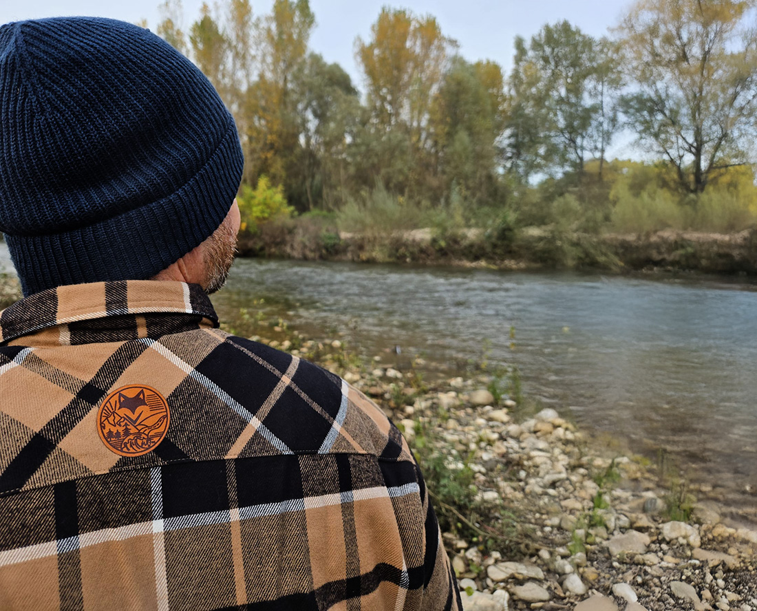 Personne au bord d’une rivière portant une veste outdoor bucheron doublé sherpa, ambiance vanlife slow