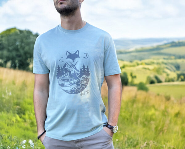 Homme portant un t-shirt rivière alpine vanlife dans un paysage vallonné.