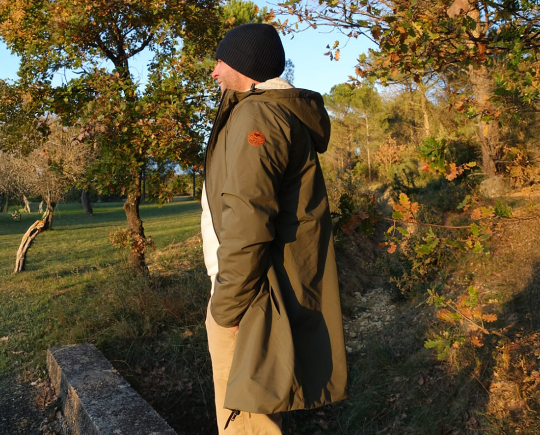 Homme portant une parka outdoor longue en forêt, vêtement écoresponsable