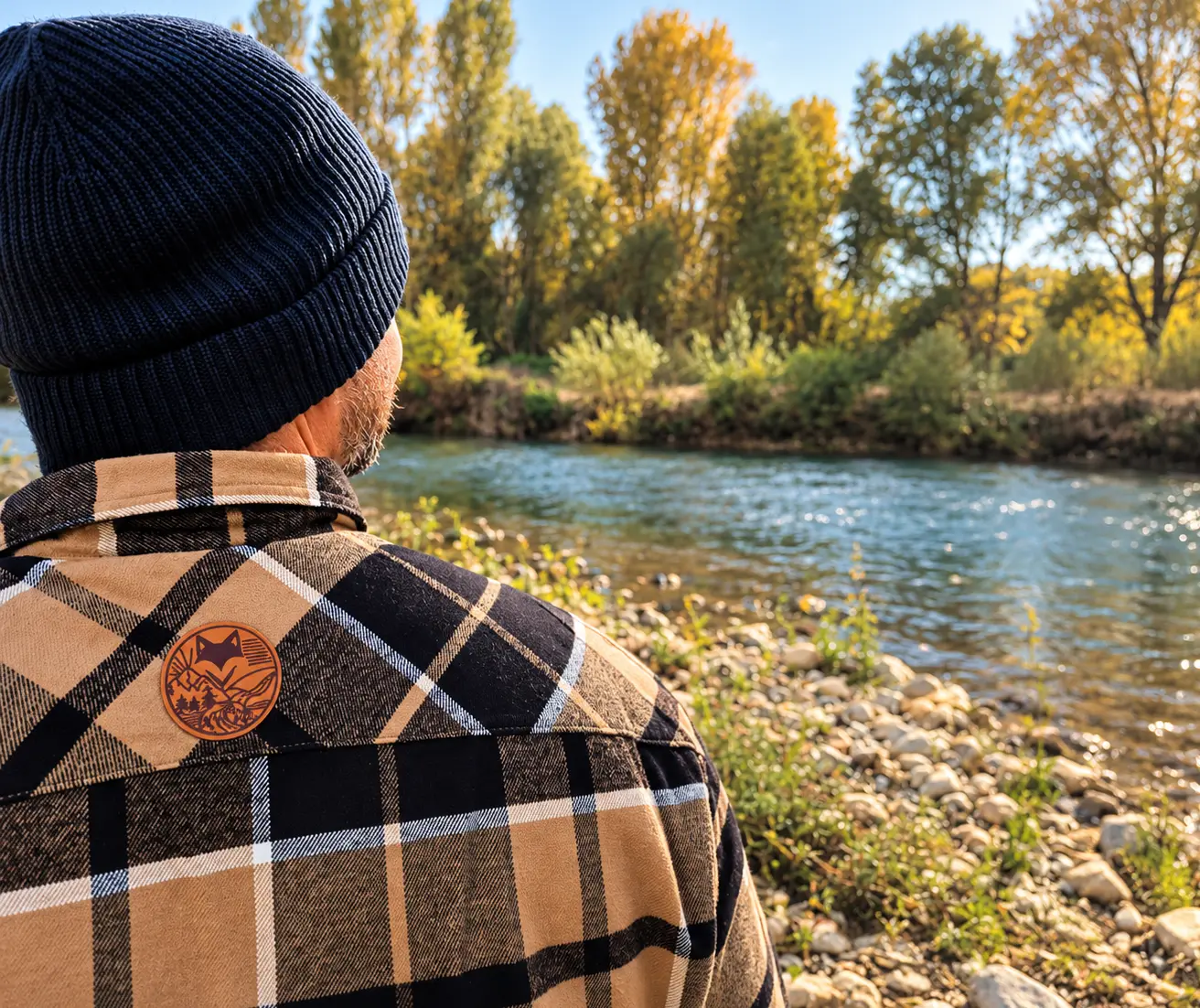 Homme portant une chemise sherpa à carreaux beige et noire au bord d'une rivière