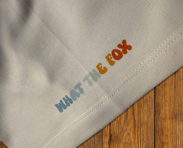 Détail “What the Fox” sur t-shirt clair, identité de marque outdoor