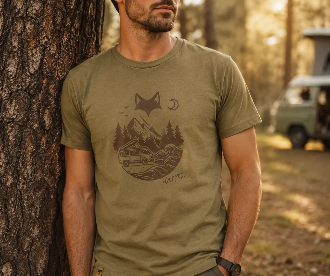 Homme portant un t-shirt van life appuyé sur un tronc d'arbre lors d'un bivouac