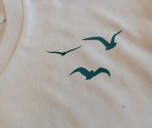 Détail visuel oiseaux sur t-shirt blanc au niveau de la clavicule qui rappelle la liberté
