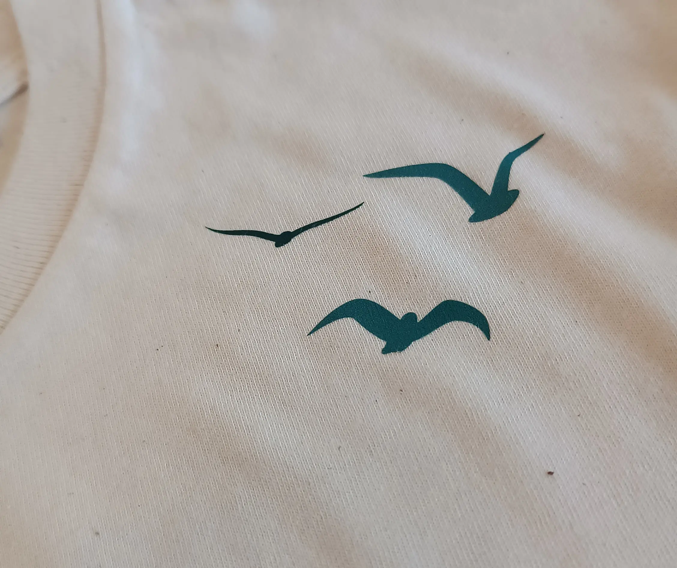 Détail visuel oiseaux sur t-shirt blanc au niveau de la clavicule qui rappelle la liberté