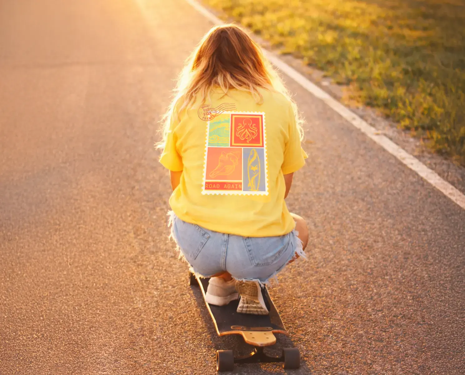 rideuse de dos qui fait du skate board portant un tee shirt bio le tee shirt est jaune ananas le visuel retro fait penser à un timbre avec des motif surfeur / van life