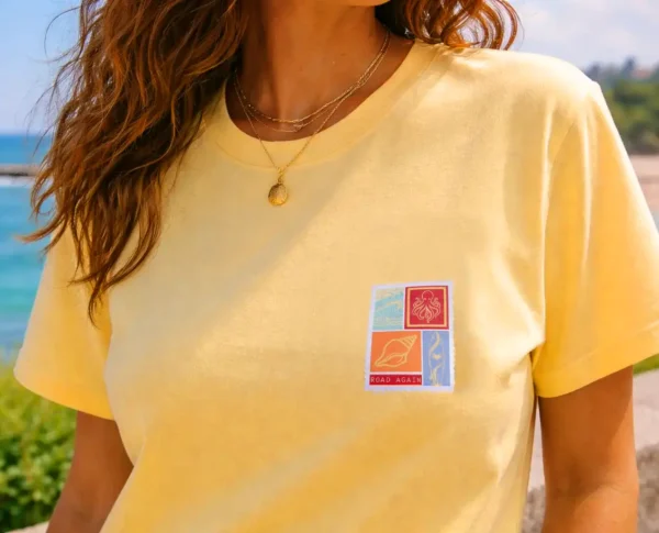 femme de face portant un tee shirt bio le tee shirt est jaune ananas le visuel retro fait penser à un timbre avec des motif surfeur / van life sur la poitrine