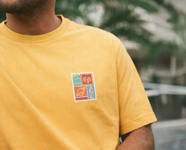 zoom sur homme de face portant un tee shirt bio le tee shirt est jaune ananas le visuel retro fait penser à un timbre avec des motif surfeur / van life sur la poitrine